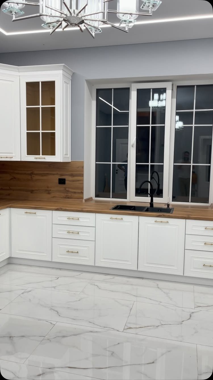 White kitchen cabinets with wooden countertops and white marble tile flooring.