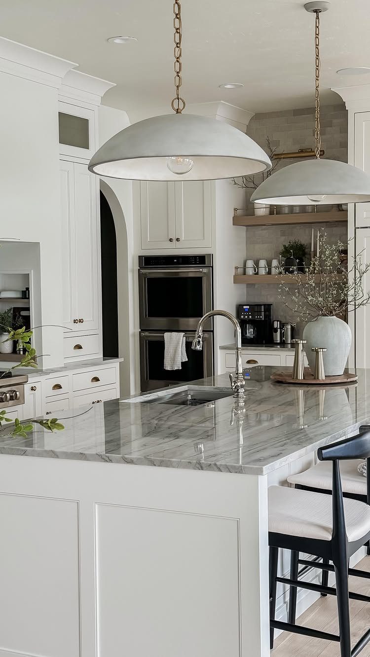 White paneled kitchen island with a grey marble countertop and dome pendant lights.