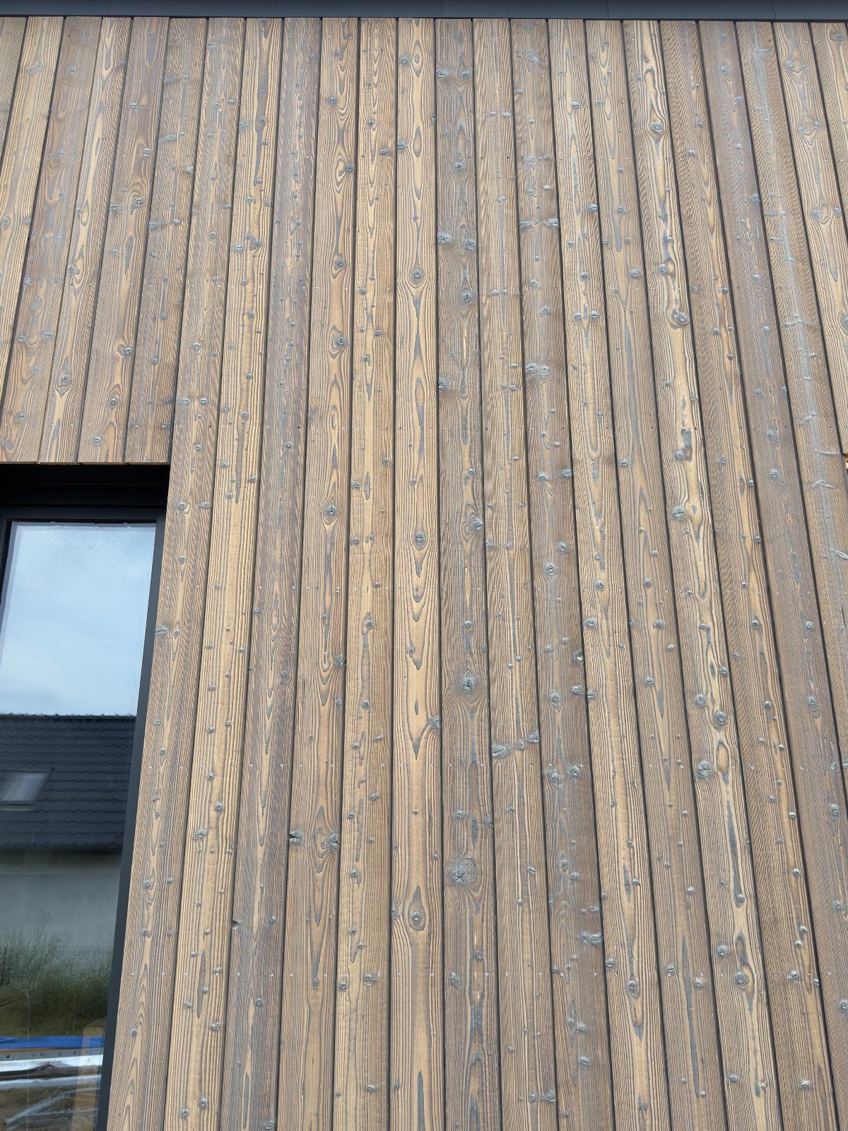 Vertical wooden slat wall on a building exterior next to a dark window frame.