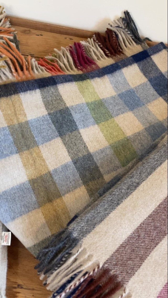 Folded wool throw blankets with plaid patterns and fringed edges on wooden surface.